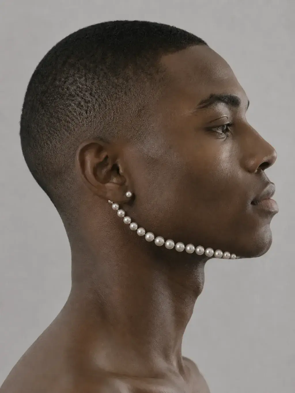 Portrait masculin de profil, rang de perles courant de l'oreille à la mâchoire comme un bijou ancré