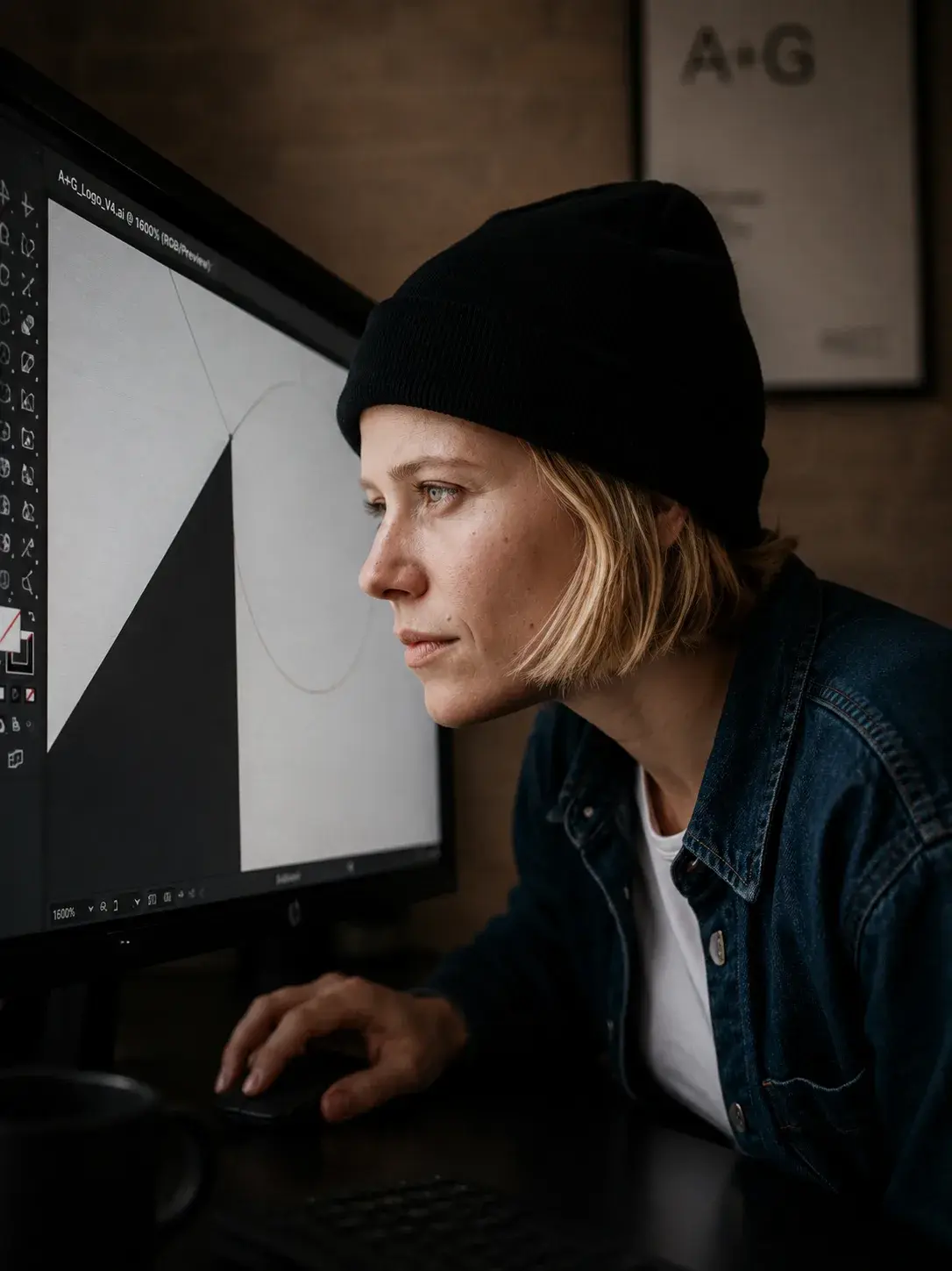 Portrait serré de profil de graphiste en bonnet noir devant écran sombre affichant logo A+G en construction sur Illustrator