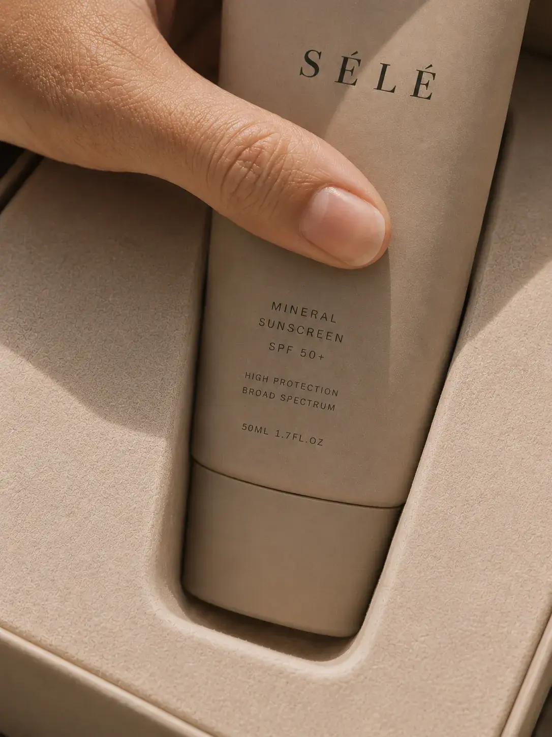 Pouce appuyant sur tube crème solaire minérale dans coffret mousse – packaging, unboxing, lumière