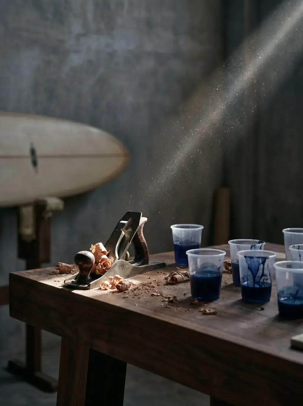 Rabot à bois et verres de pigment bleu sur établi d'atelier avec planche de surf en fond