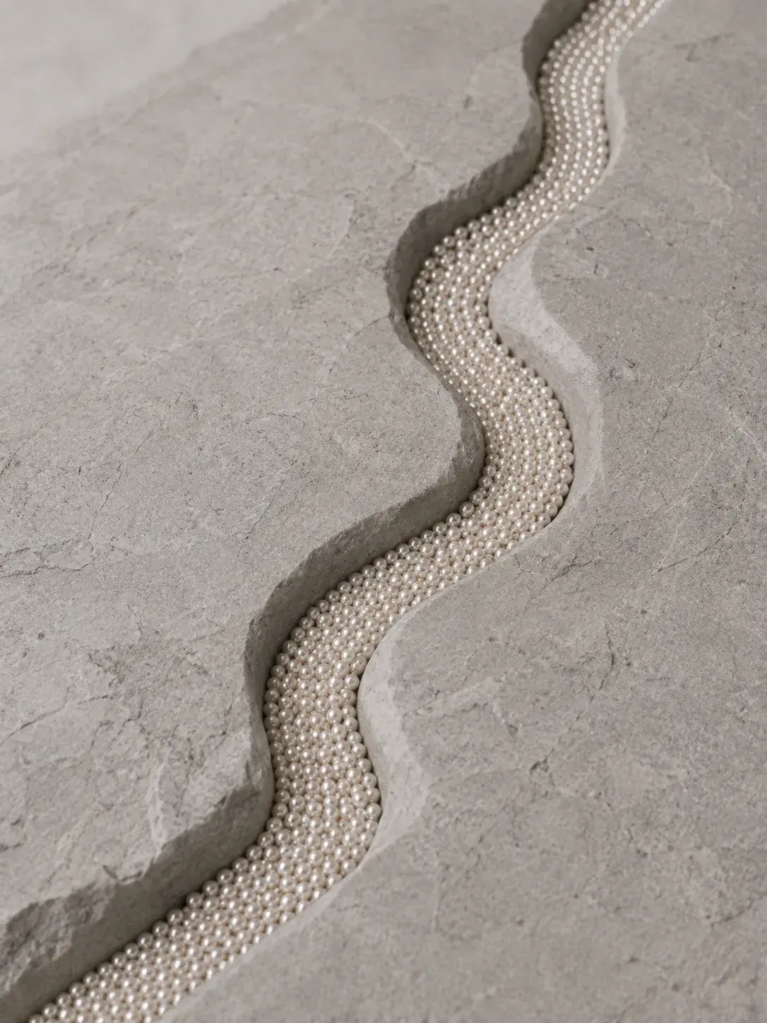 Rang de perles calibrées niché dans une fissure sinusoïdale taillée dans la pierre grise, bijou minéral