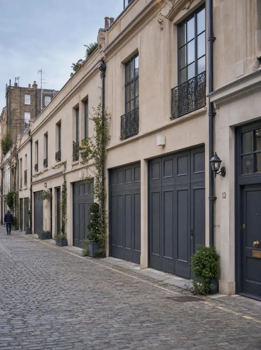 Ruelle de mews londonien avec maisons de ville beige à portes de garage anthracite et plantes grimpantes