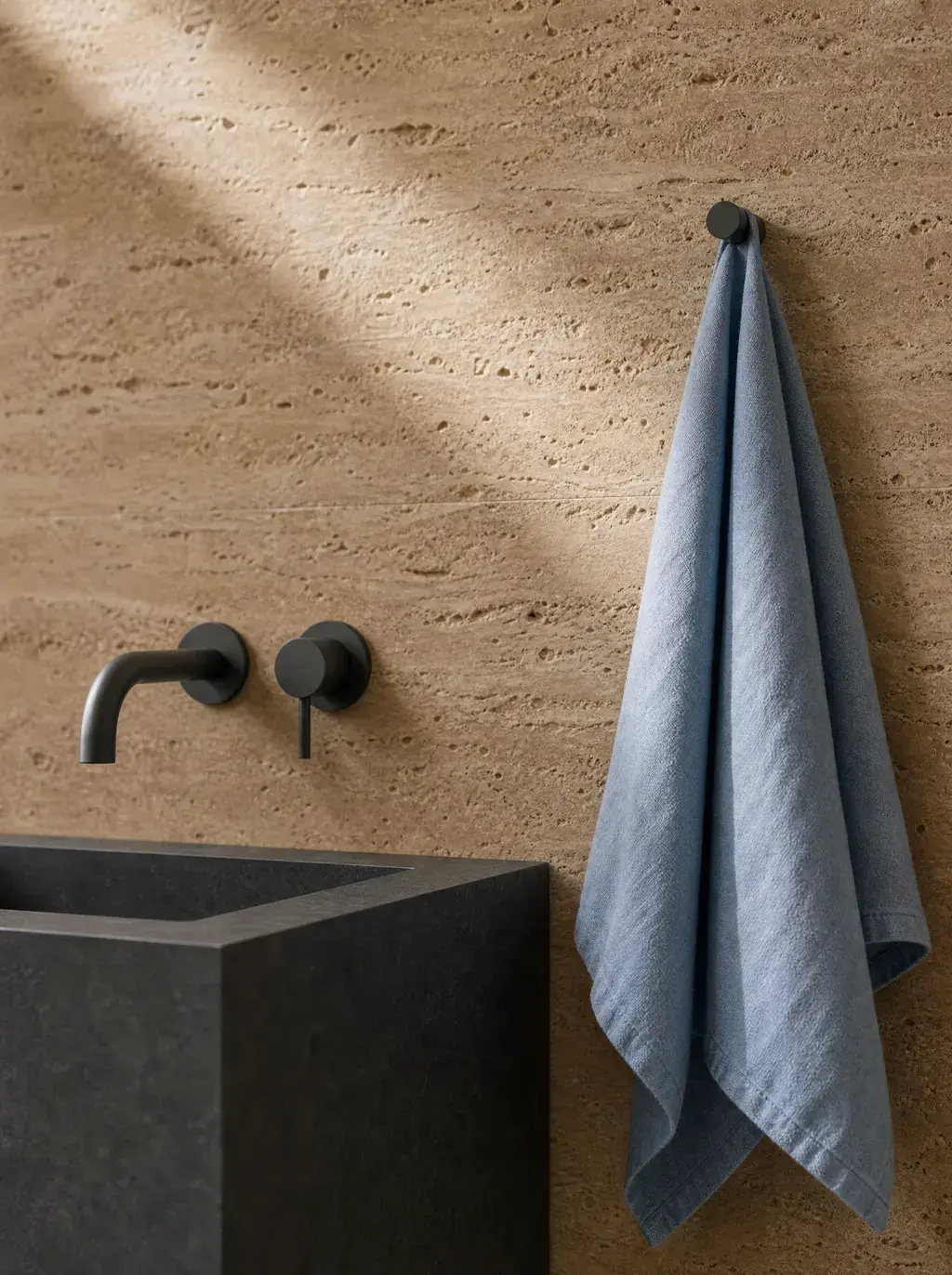 Salle de bain minimaliste avec vasque en béton, robinetterie encastrée et serviette en lin bleu sur travertin