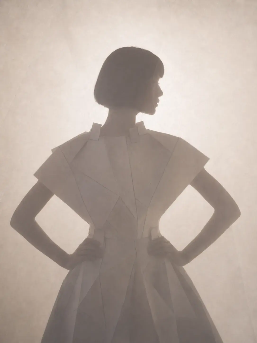 Silhouette de femme en robe géométrique blanche de dos – fond brumeux et éthéré