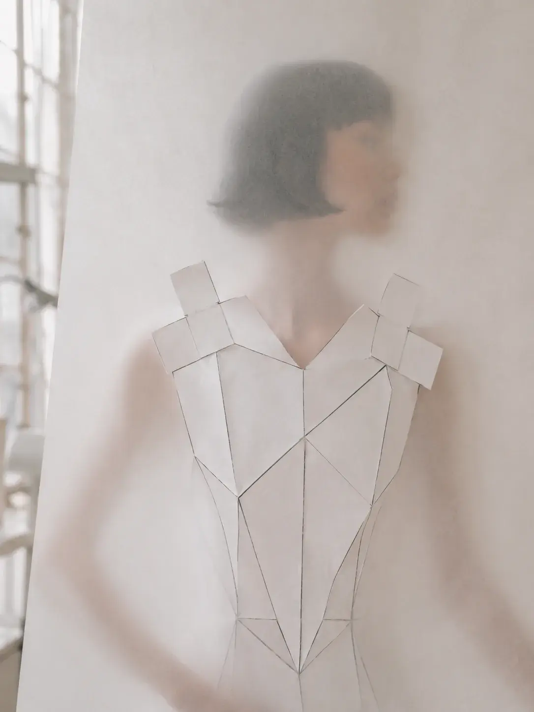 Silhouette féminine en robe origami projetée sur voile translucide – lumière diffuse