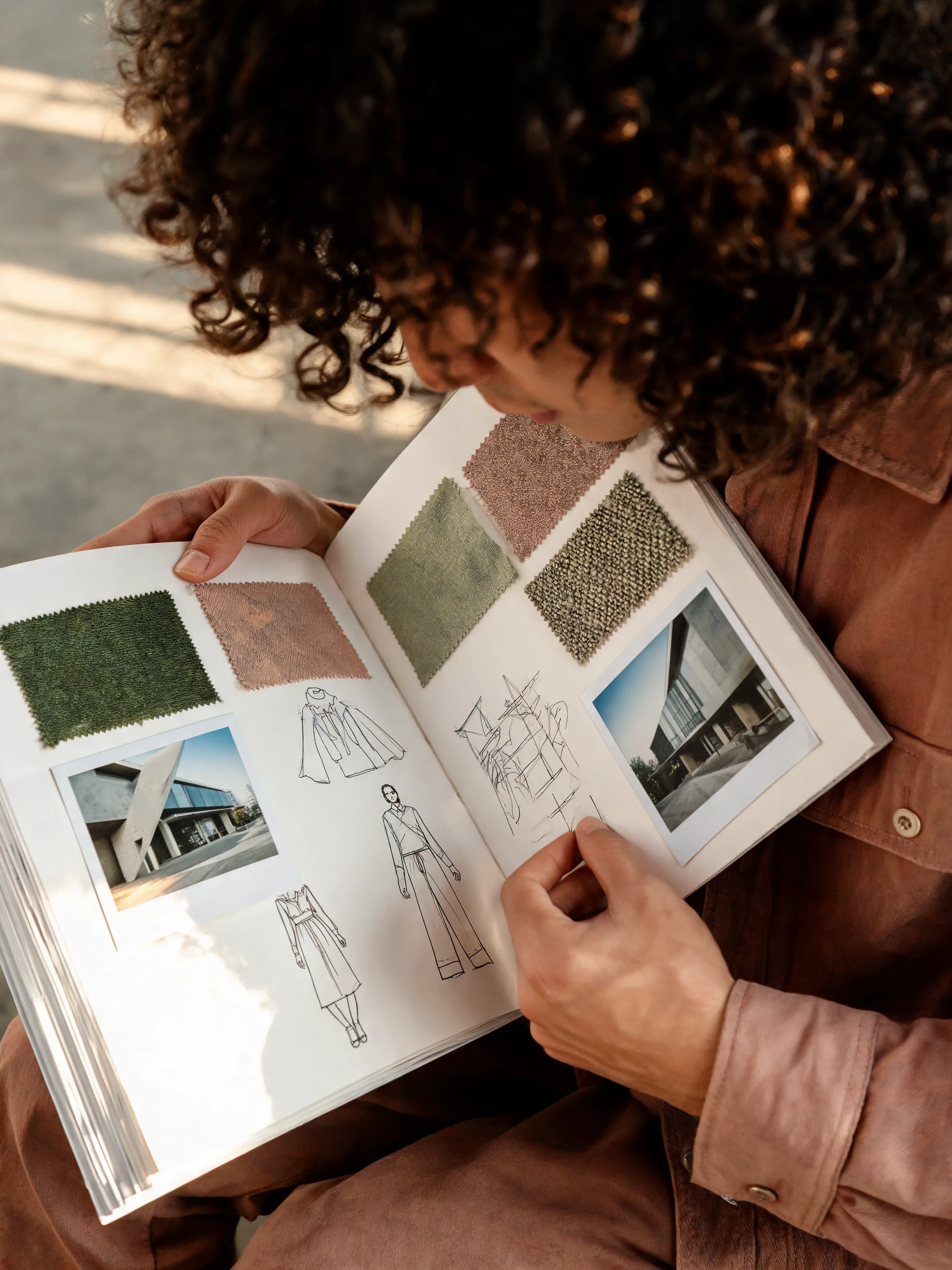 Styliste feuilletant carnet de référence – croquis silhouettes mode, échantillons tissu, photos boutique