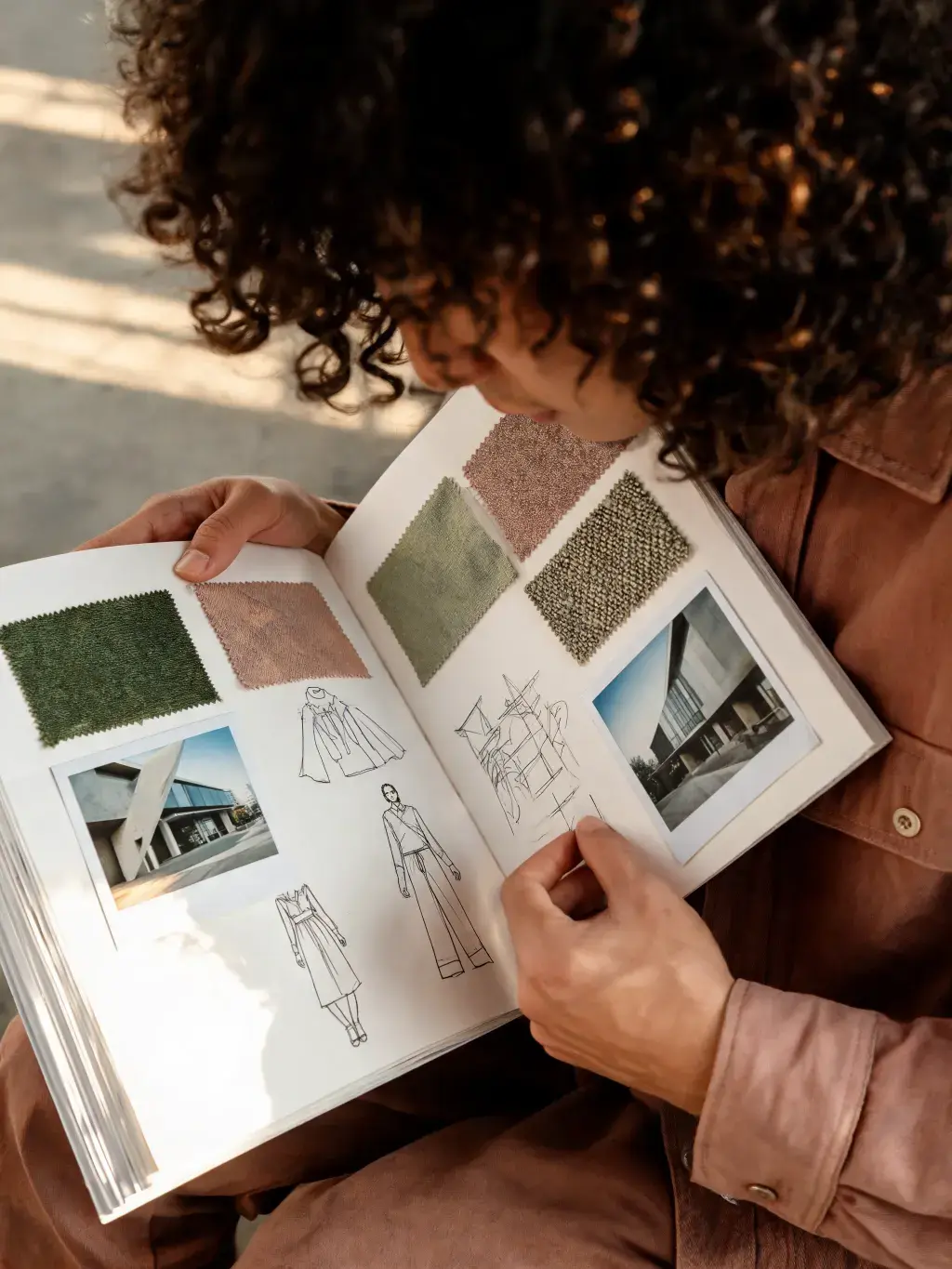 Styliste feuilletant carnet de référence – croquis silhouettes mode, échantillons tissu, photos boutique