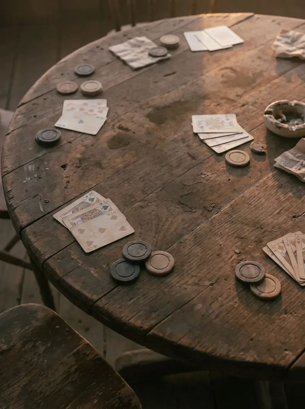 Table ronde de saloon en bois avec cartes à jouer dispersées et jetons de poker en ambiance sombre