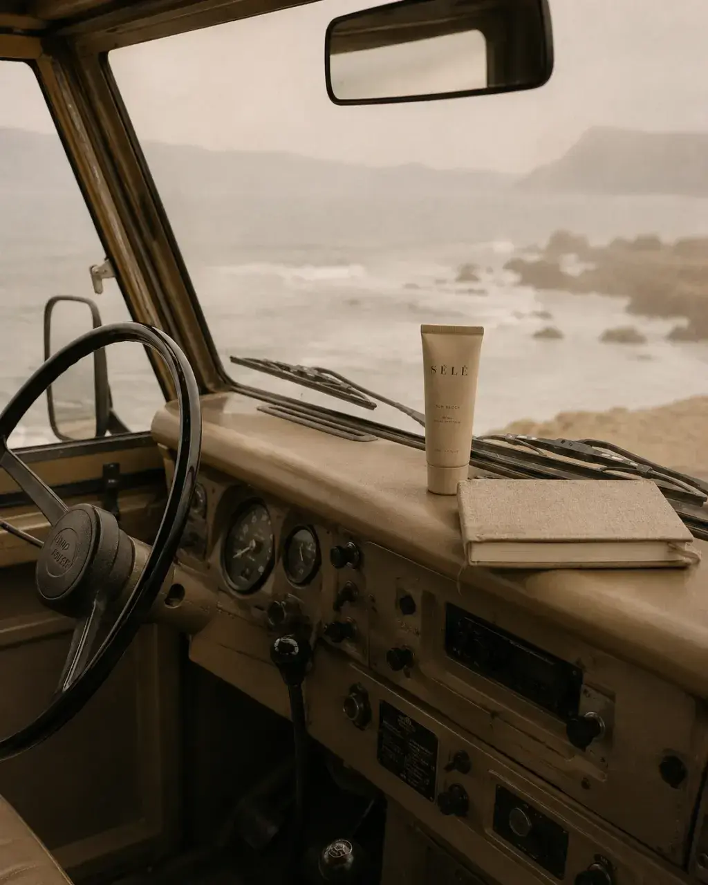 Tableau de bord 4x4 vintage – tube crème solaire sur carnet, mer agitée par le pare-brise, road trip