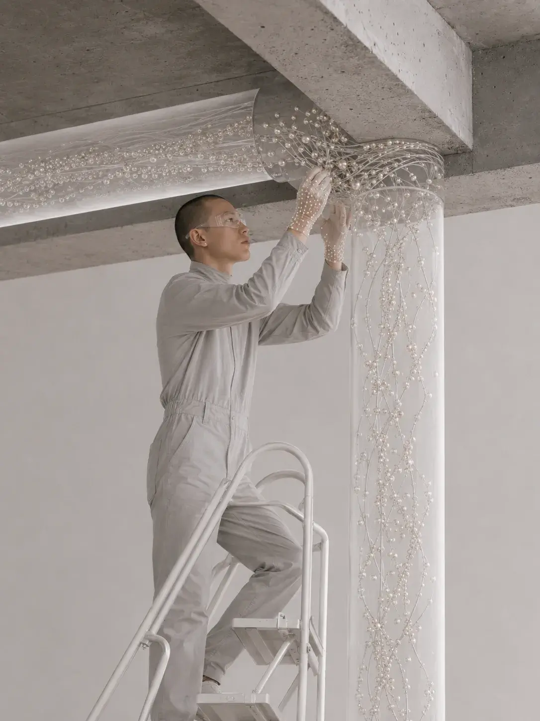 Technicien sur escabeau incrustant des perles à la jonction plafond-colonne d'un espace en béton