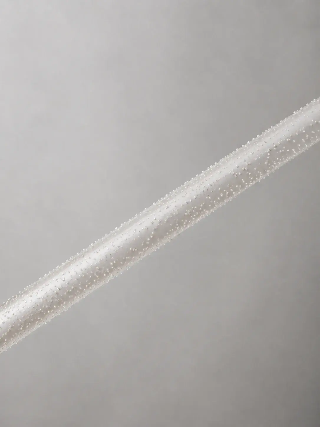 Tige fine recouverte de micro-perles sur toute sa longueur, composition diagonale minimaliste fond gris