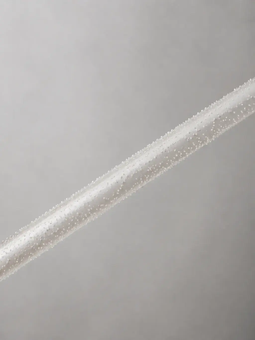 Tige fine recouverte de micro-perles sur toute sa longueur, composition diagonale minimaliste fond gris