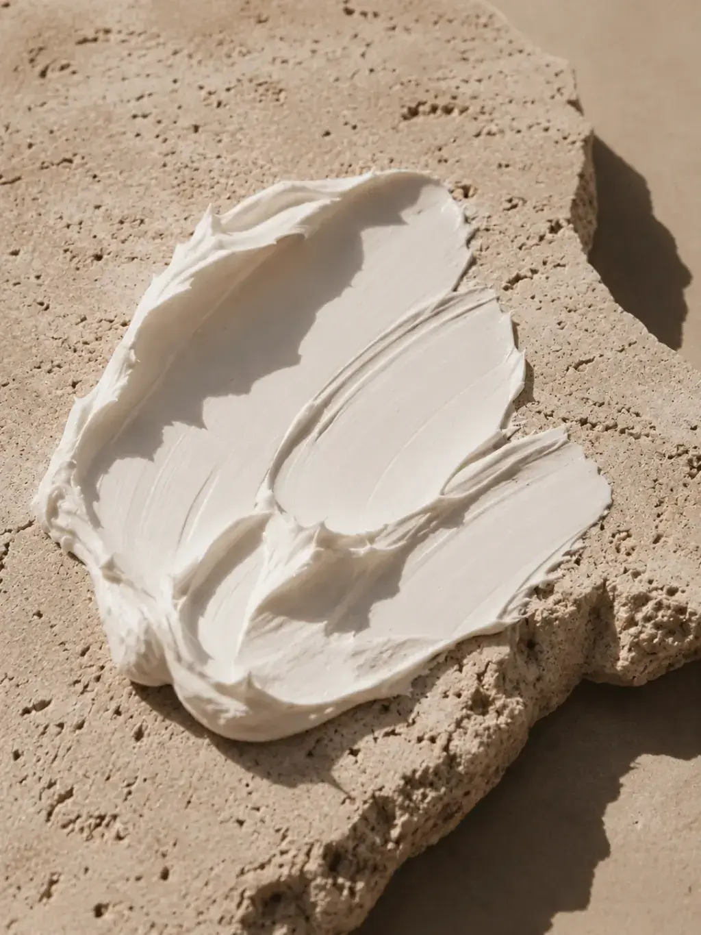 Trace épaisse de crème blanche sur bloc de pierre calcaire – texture sable, désert, lumière rasante