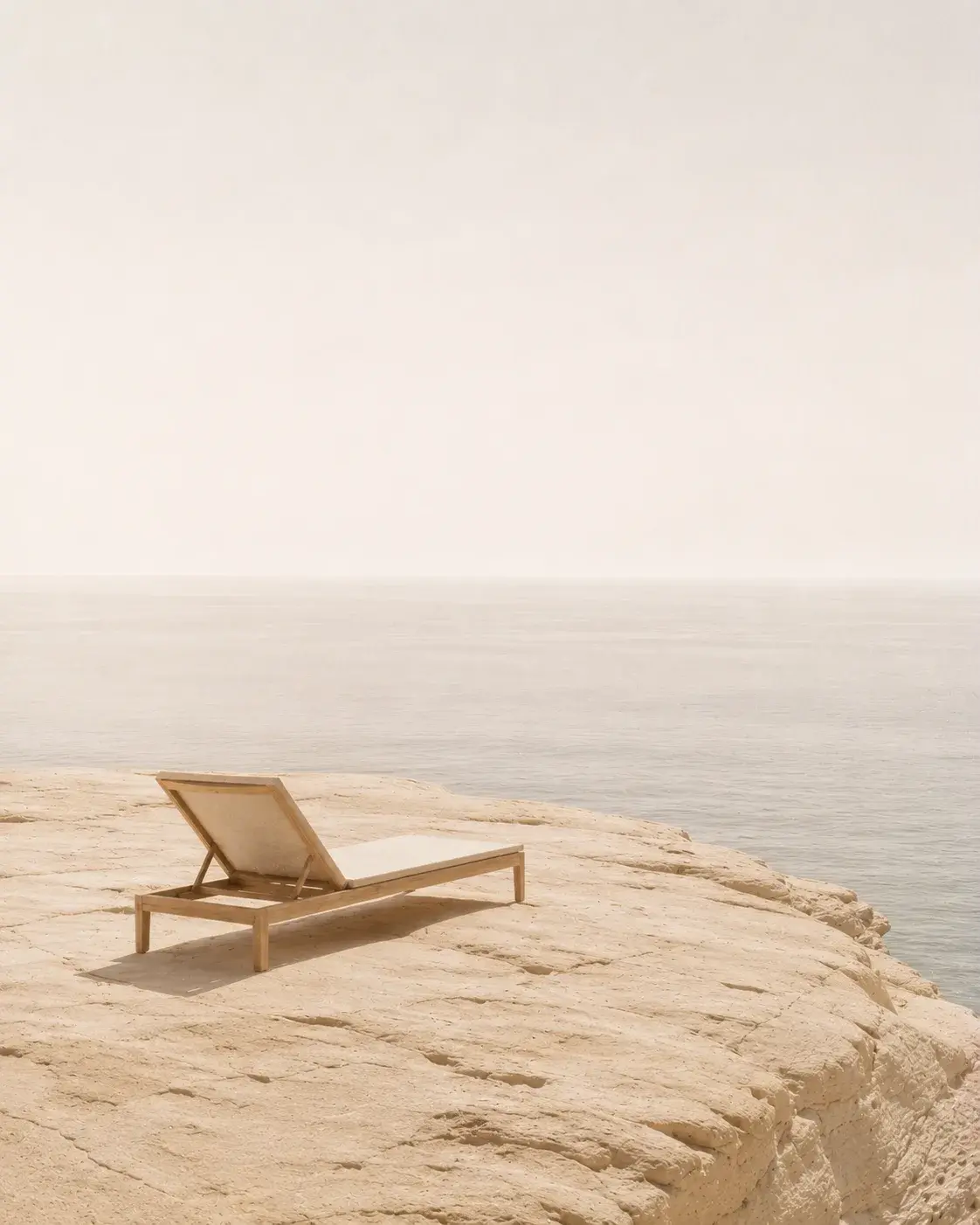 Transat en bois naturel posé sur rocher face à la mer – minimalisme côtier lumineux