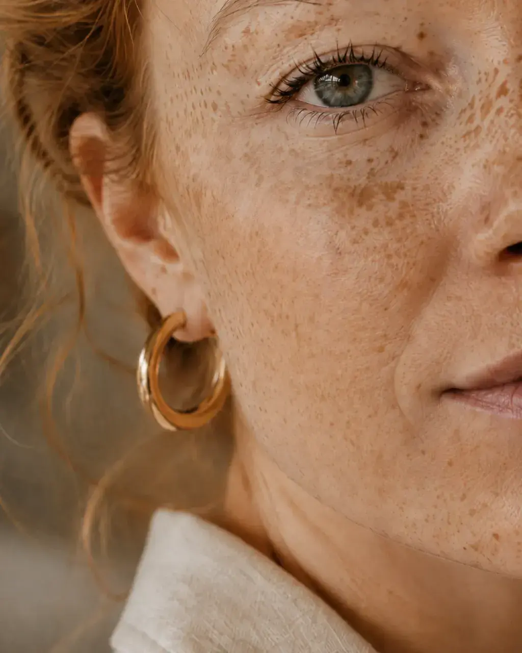 Très gros plan demi-visage femme rousse aux taches de rousseur – œil vert et boucle d'oreille dorée