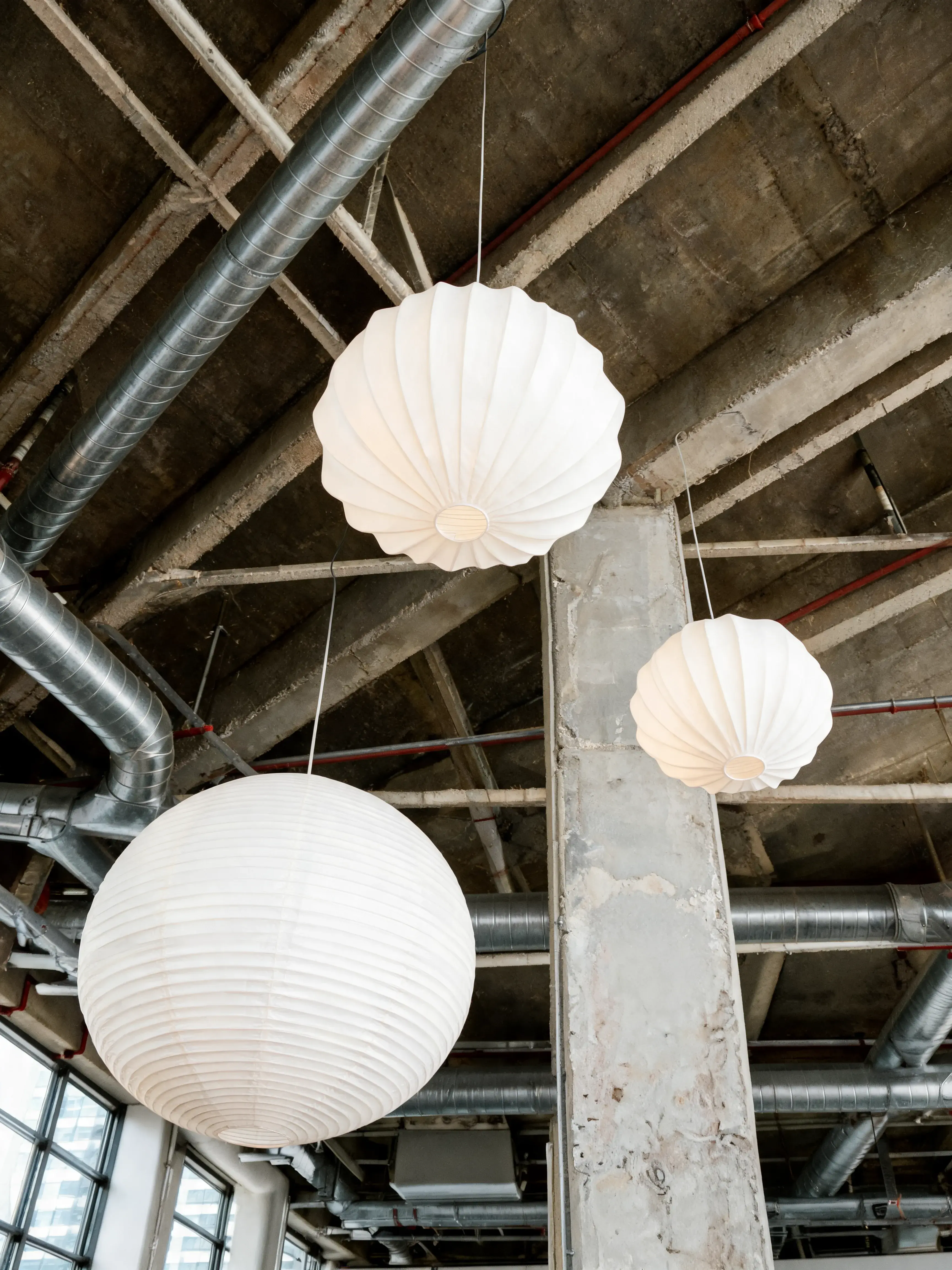 Trois lampes globe blanc suspendues – plafond béton tuyaux industriels, pilier, loft