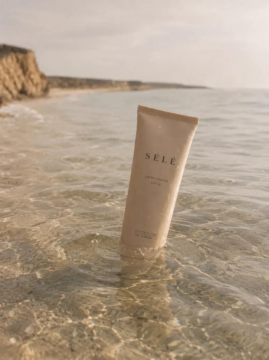 Tube crème solaire beige dressé dans eau peu profonde sur plage – falaises, mer, ciel nuageux