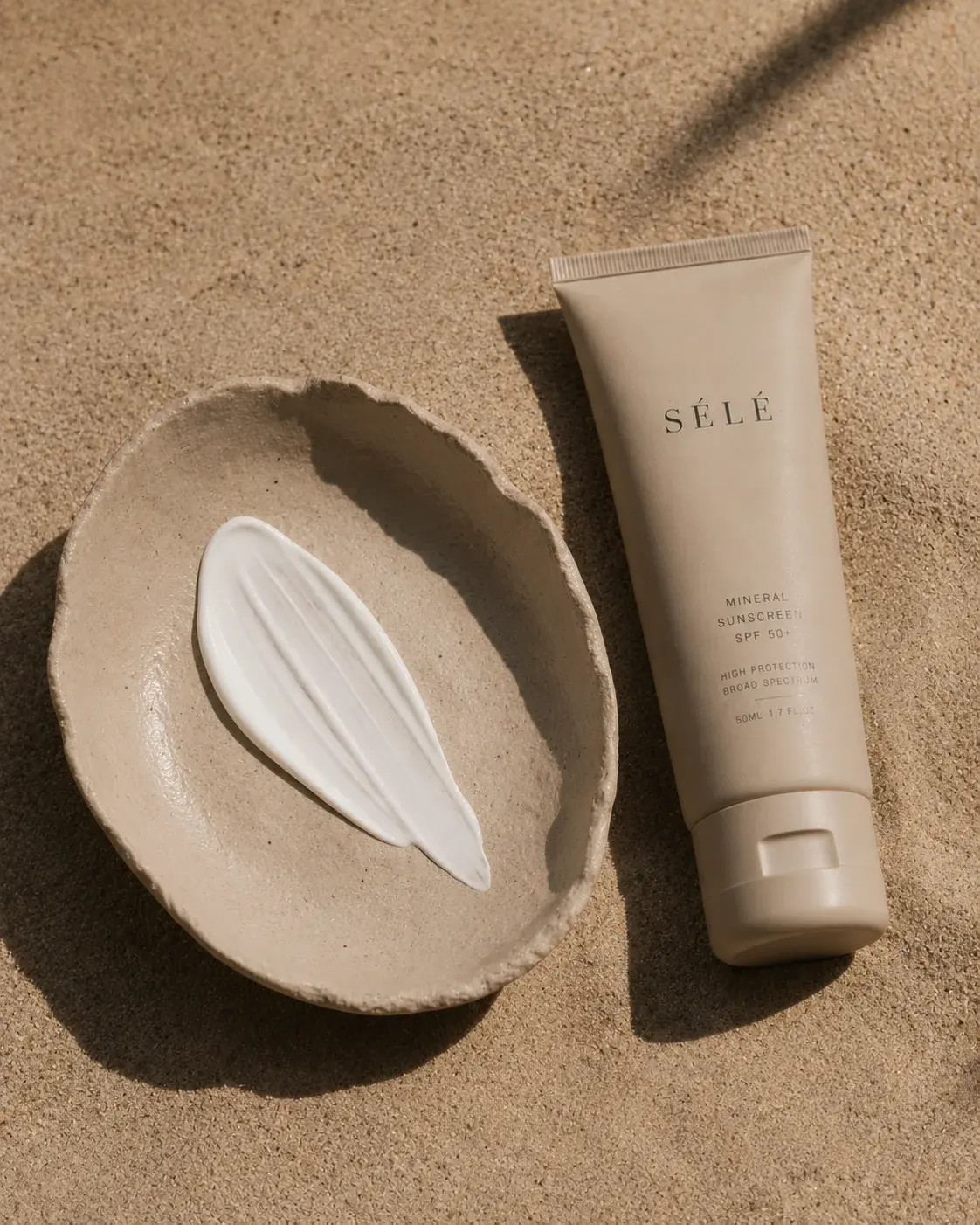 Tube crème solaire beige et bol céramique avec trace crème – sable désertique, lumière rasante