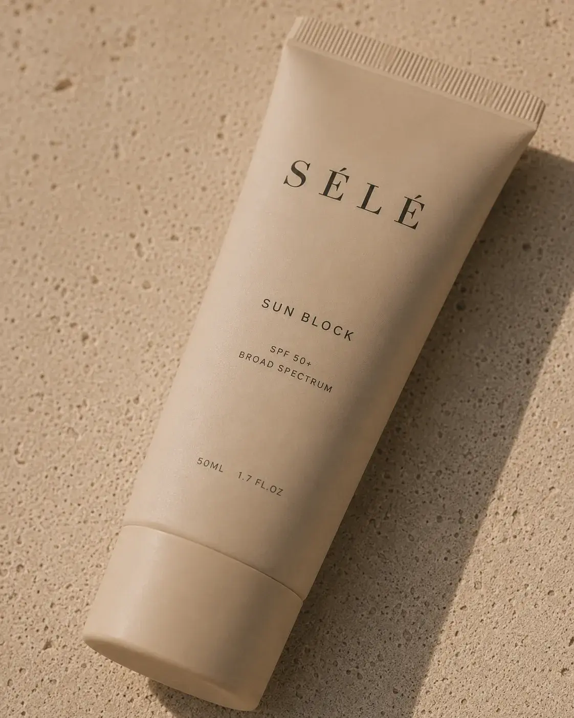 Tube crème solaire beige mat posé sur travertin texturé – lumière rasante, ombre portée, fond neutre