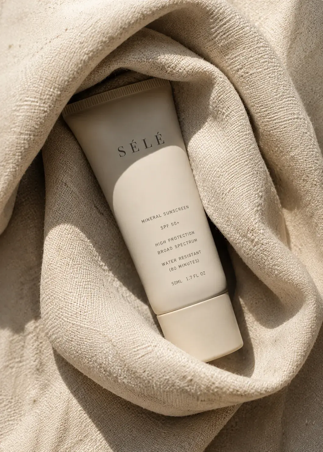 Tube crème solaire blanc posé dans tissu éponge beige froissé – lumière douce, ombre