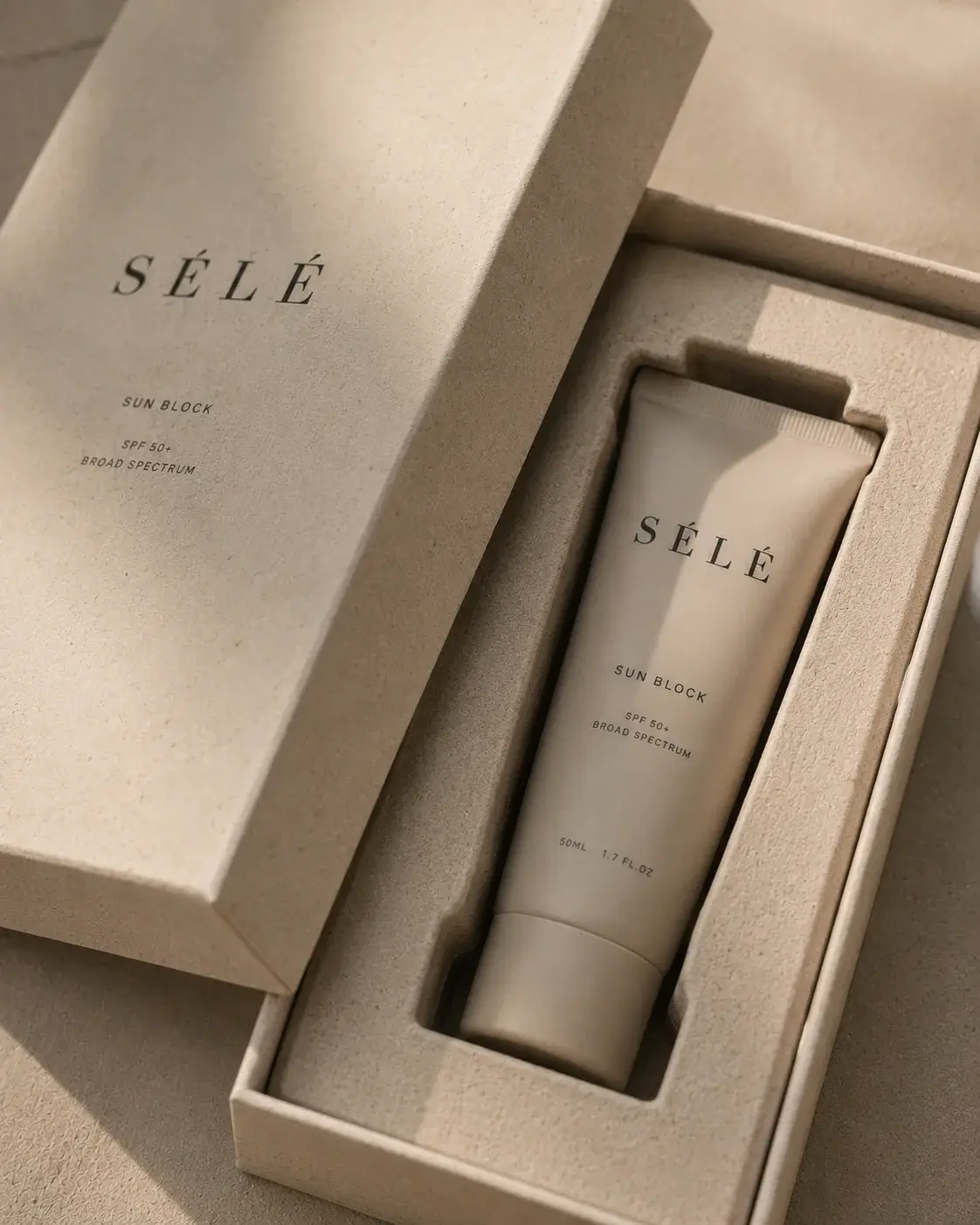 Tube crème solaire dans coffret kraft ouvert – packaging luxe, papier de soie, lumière douce