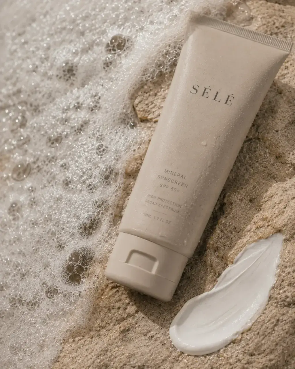 Tube crème solaire minérale sur sable mouillé avec écume – trace de crème, vague, plage, lumière