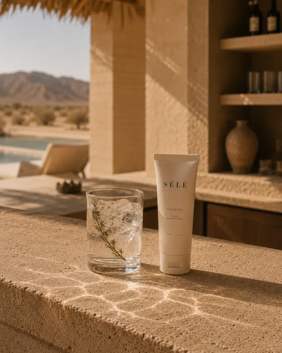Tube de soin solaire avec verre d'eau glacé – villa resort désertique en arrière-plan