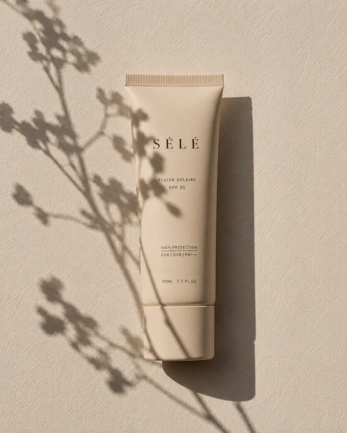 Tube fluide solaire beige sur mur plâtre – ombre de fleurs sauvages, lumière rasante, fond neutre