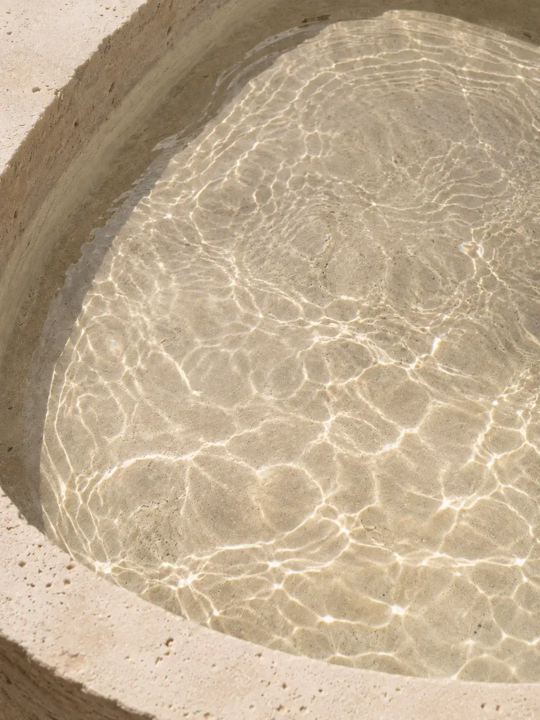 Vasque en pierre naturelle avec eau cristalline – reflets lumineux sur surface