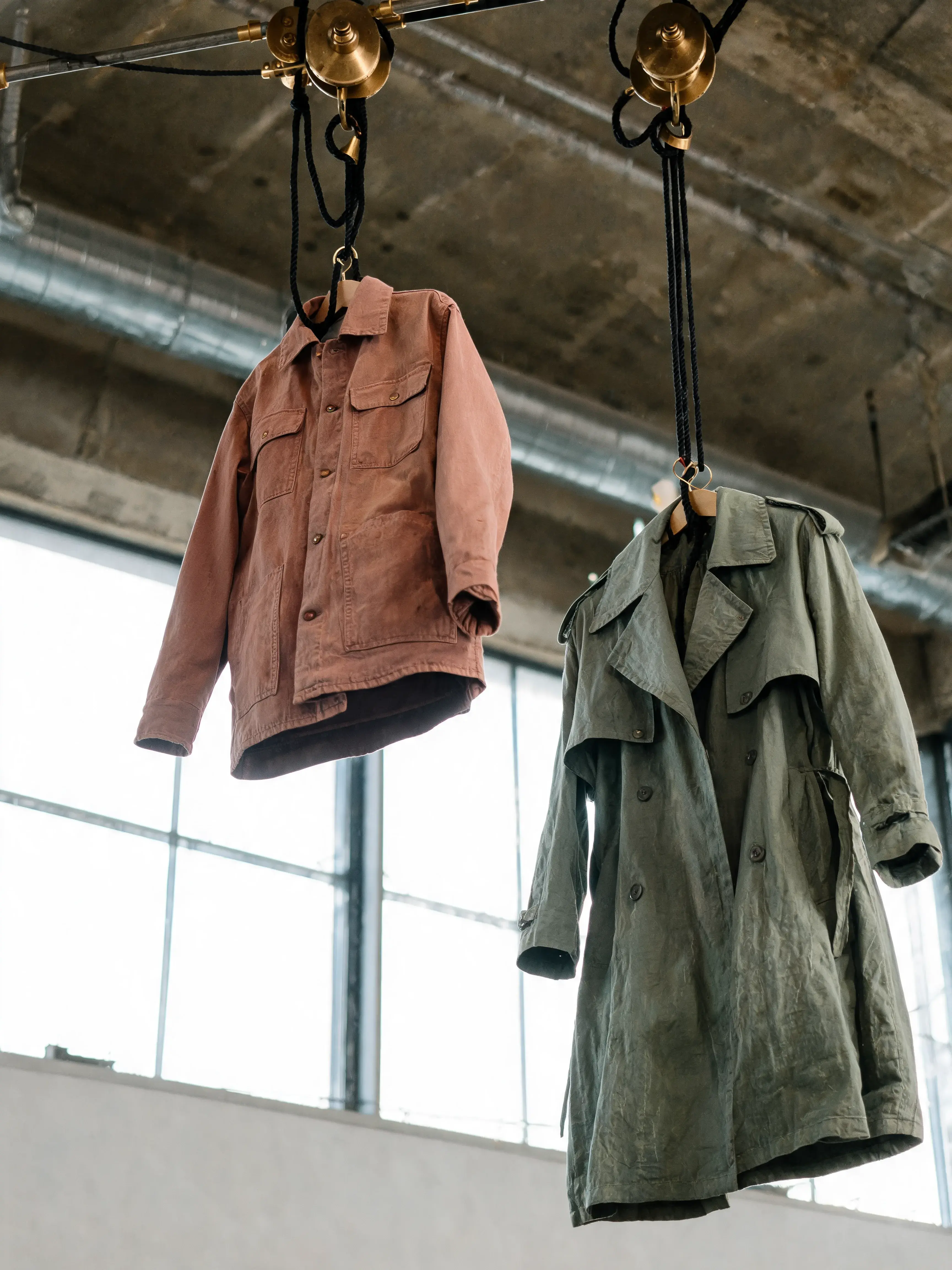 Veste terracotta et trench vert suspendus câbles laiton poulies – fenêtre atelier, contre-jour