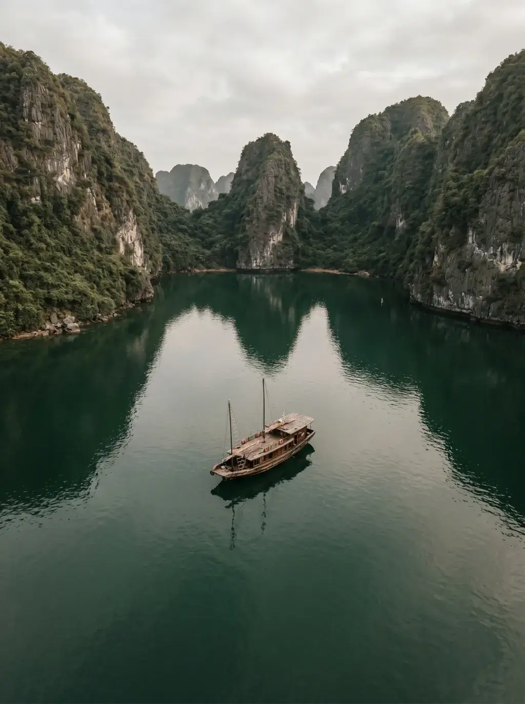 Vue aérienne de la Baie d'Halong — jonque solitaire reflétée dans l'eau émeraude entre karsts couverts de végétation
