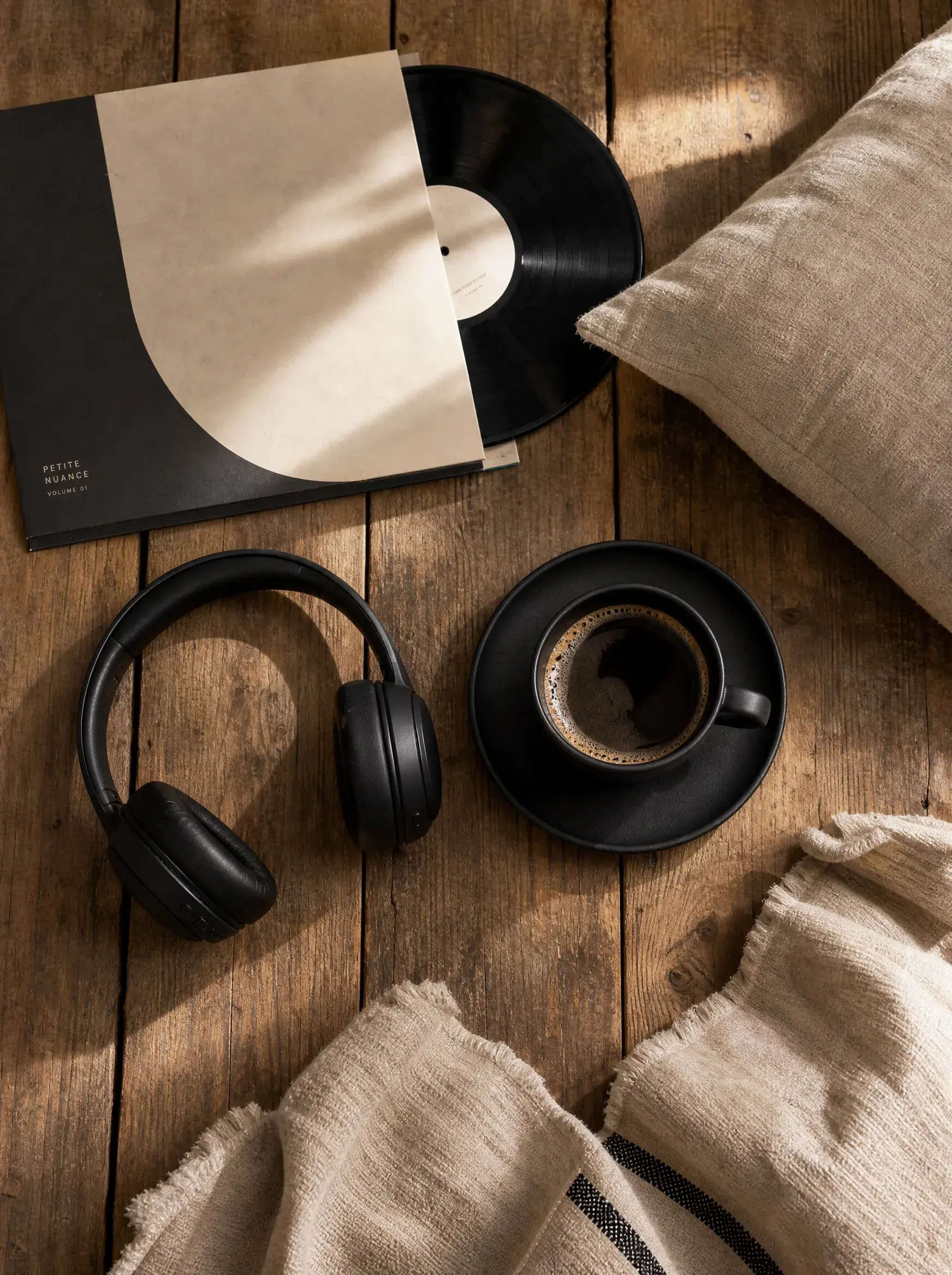Vue aérienne – disque vinyle kraft, casque audio noir, espresso, lin, plancher bois sombre
