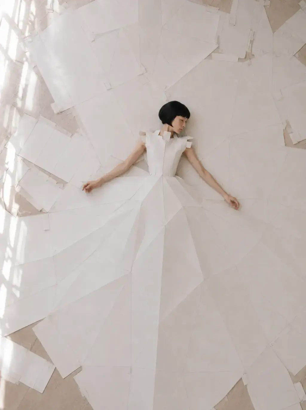 Vue aérienne femme en robe origami allongée sur sol de papiers déchirés – studio lumière rasante