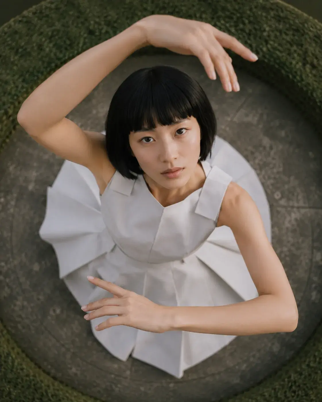 Vue aérienne femme en robe origami dans arche de buis circulaire – regard caméra du dessus