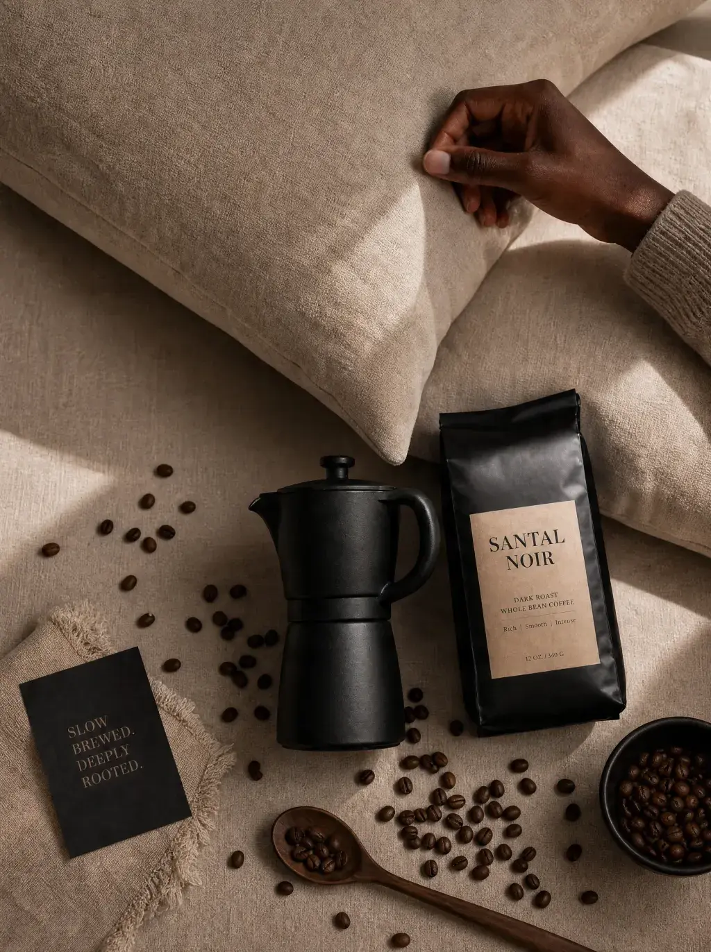 Vue aérienne lit – main, sachet café artisanal noir, cafetière moka, cuillère grains, lin beige