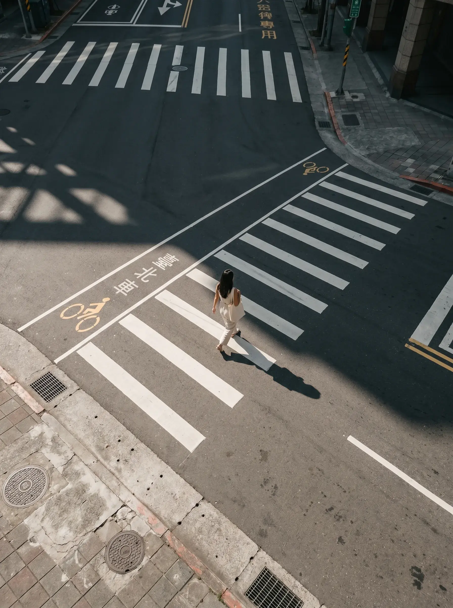 Vue aérienne plongeante sur femme seule traversant une intersection avec caractères chinois à Taipei, ombres nettes au sol