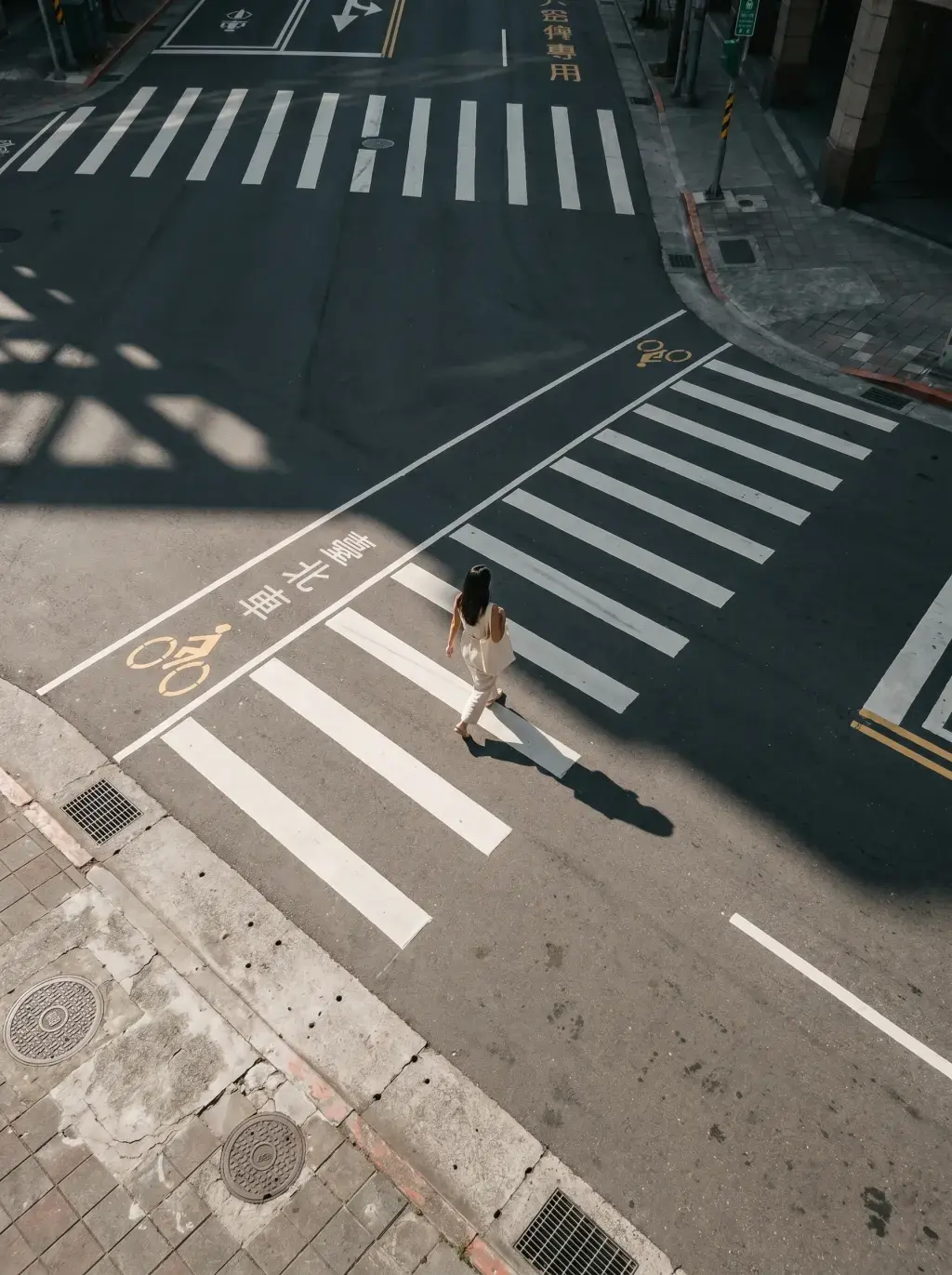Vue aérienne plongeante sur femme seule traversant une intersection avec caractères chinois à Taipei, ombres nettes au sol