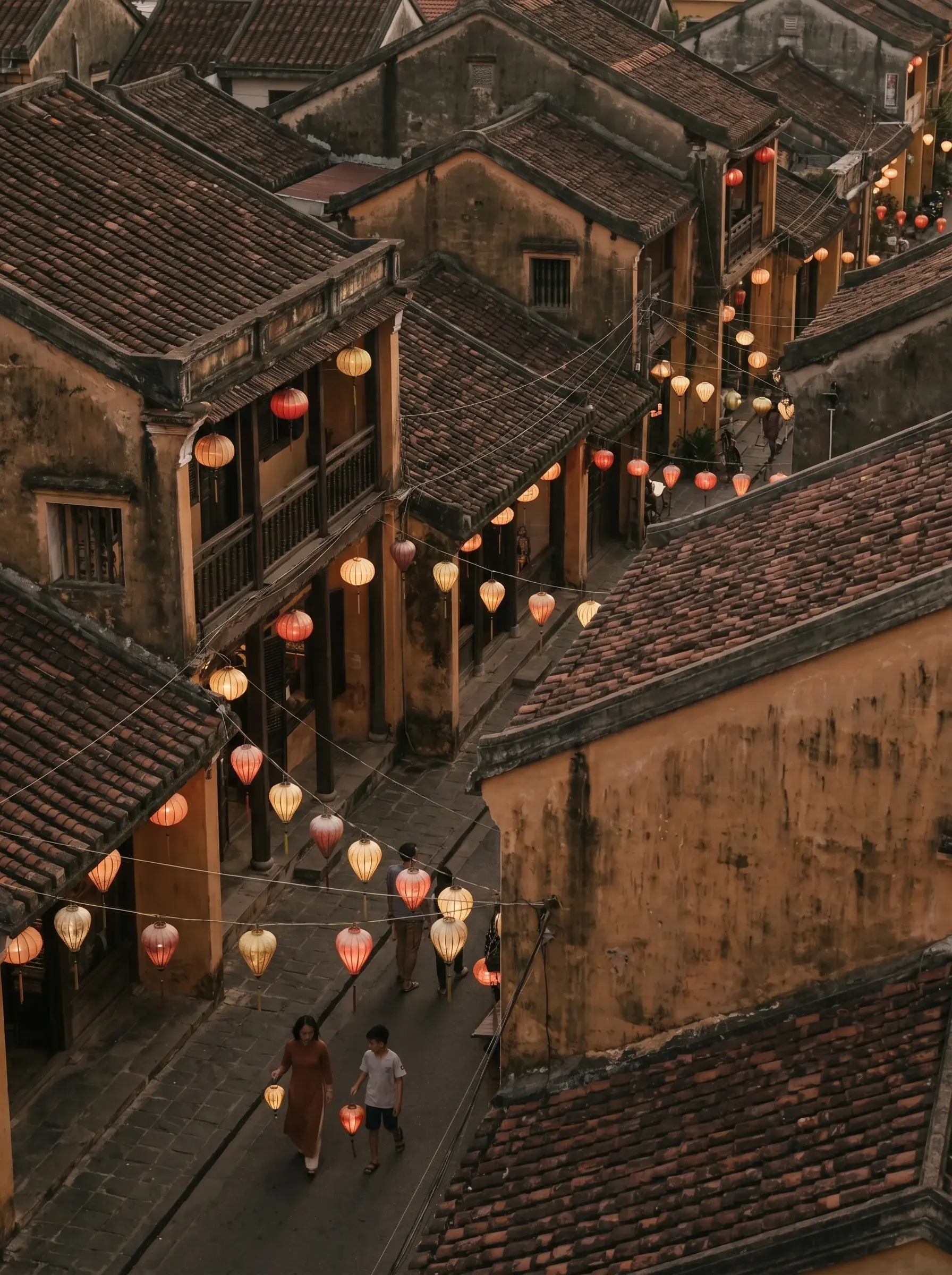 Vue aérienne sur toits et ruelles de la vieille ville de Hội An avec lanternes colorées allumées et deux silhouettes au sol