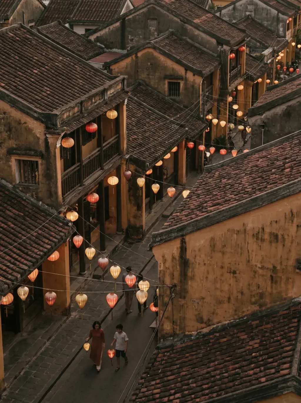 Vue aérienne sur toits et ruelles de la vieille ville de Hội An avec lanternes colorées allumées et deux silhouettes au sol