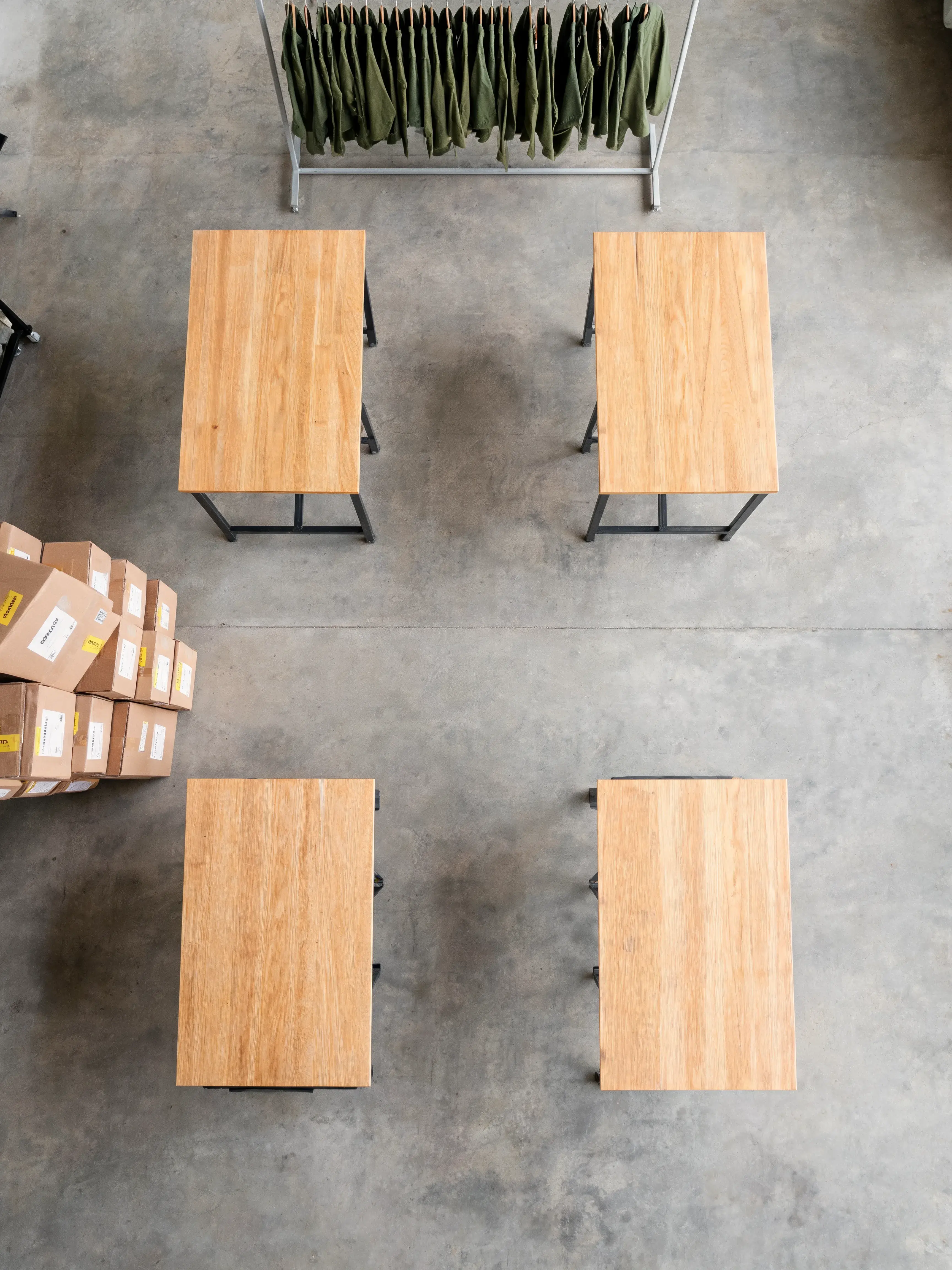 Vue aérienne tables bois et portant vêtements verts – cartons, sol béton, entrepôt mode