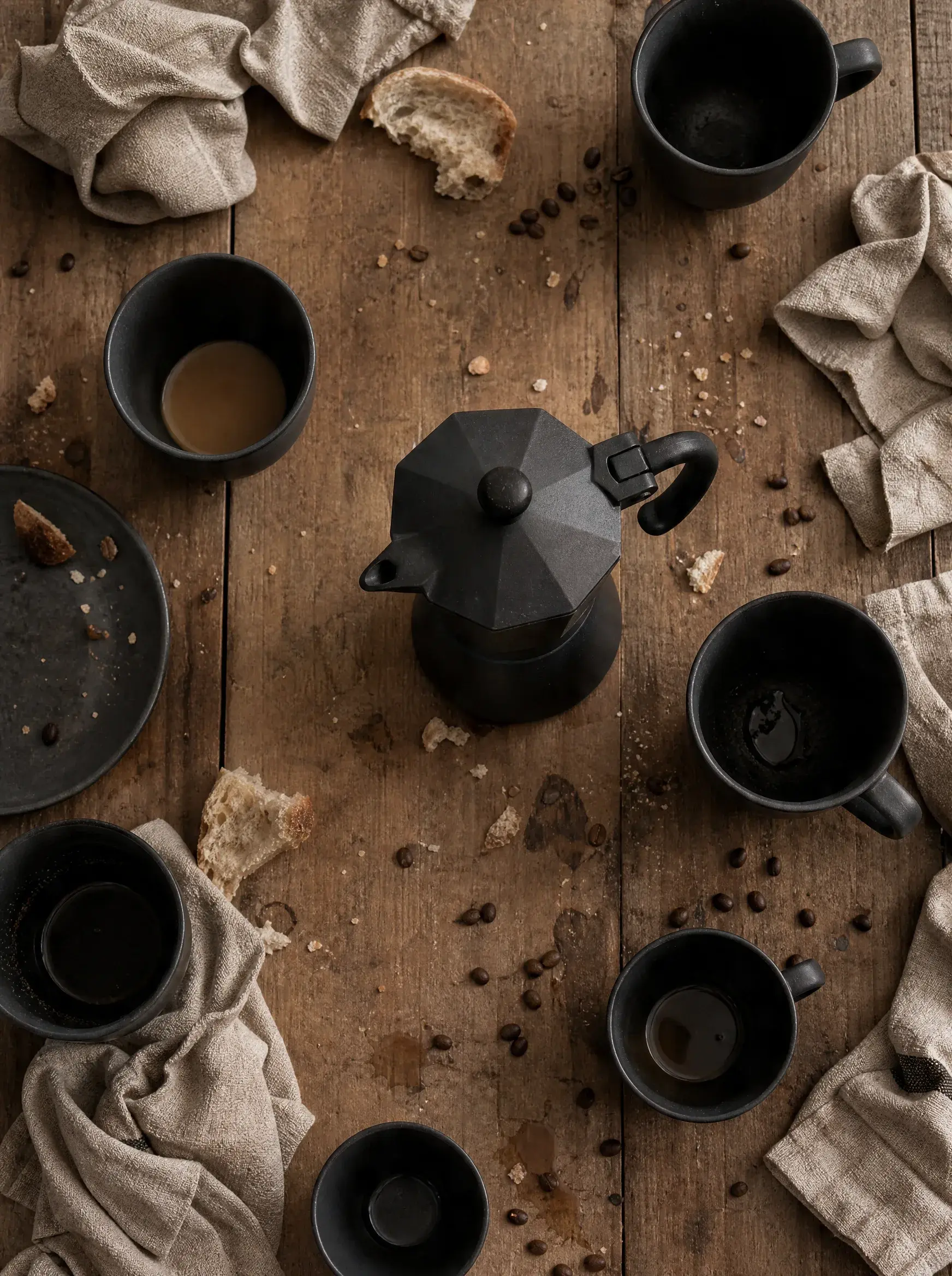Vue de dessus – cafetière moka, six mugs noirs, pain, nappe lin, table bois – rassemblement convivial