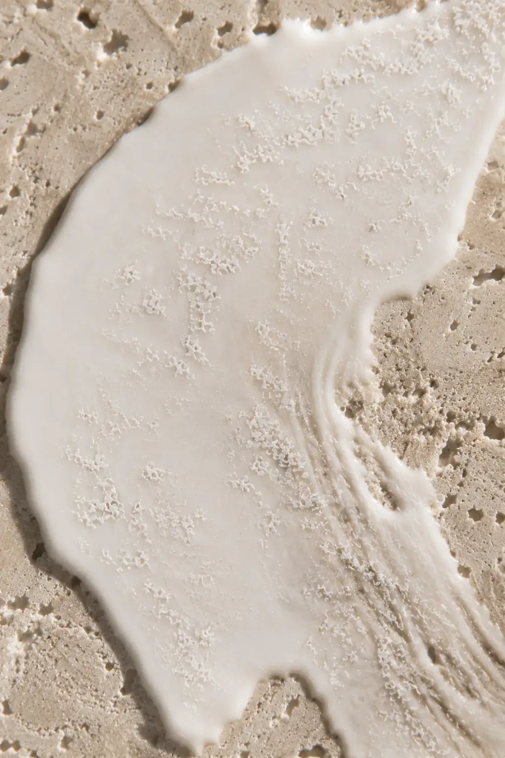 Vue de dessus crème blanche étalée sur travertin – microparticules, texture minérale, lumière douce