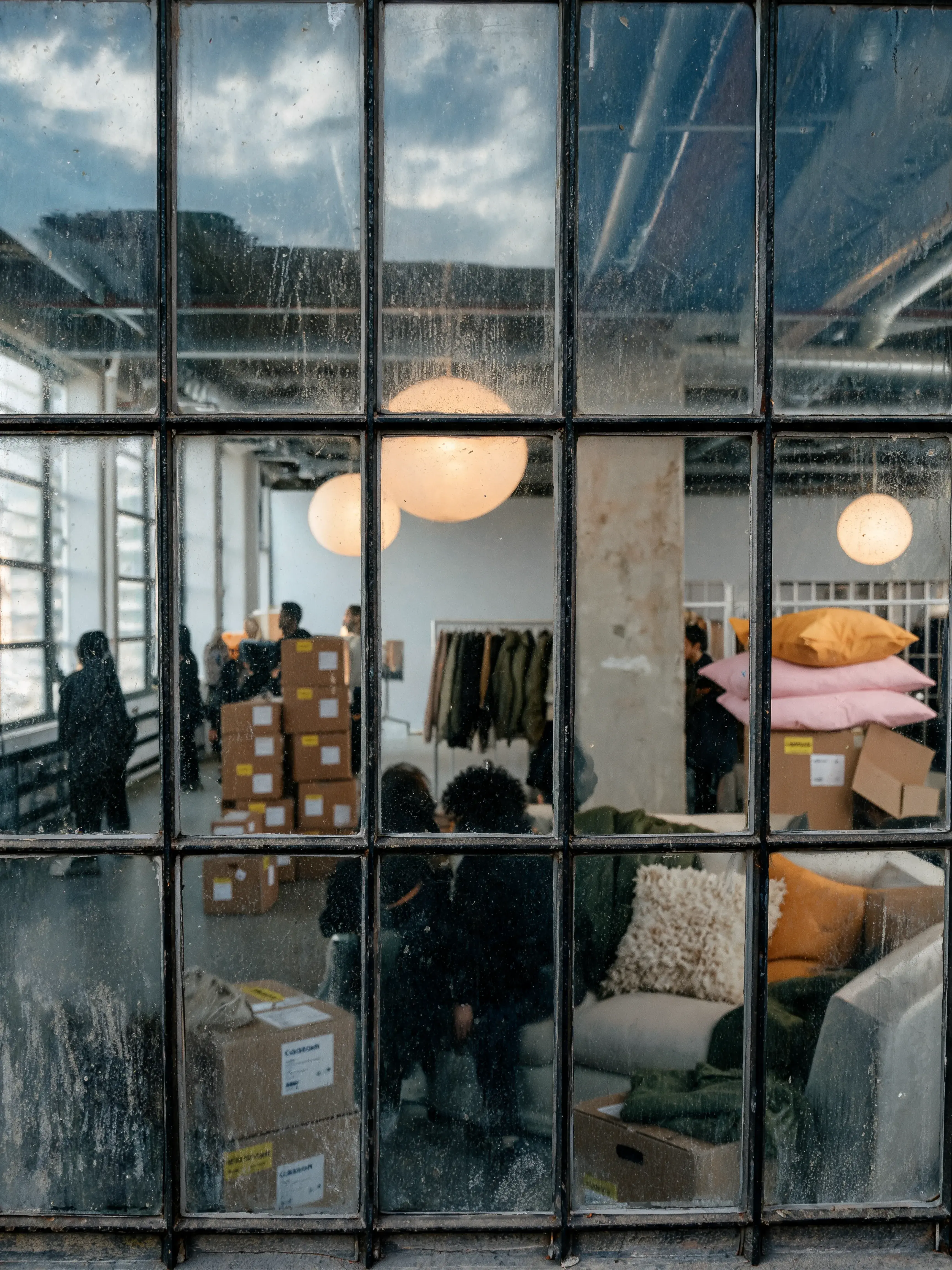Vue extérieure fenêtres industrielles – équipe en activité, cartons, coussins, intérieur loft