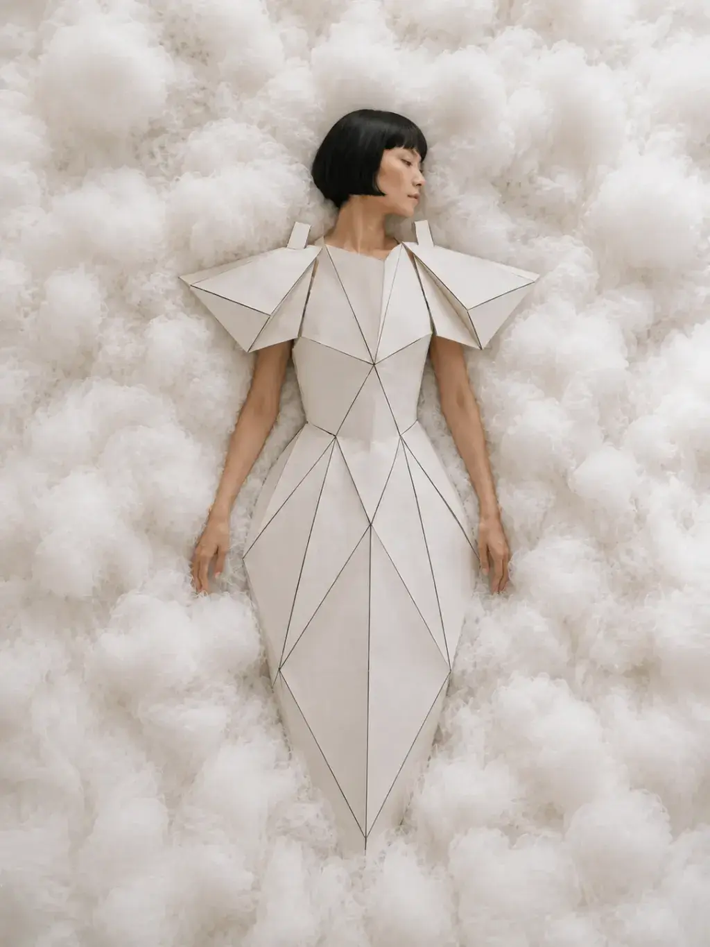 Vue plongeante – femme en robe géométrique blanche allongée dans des nuages de coton