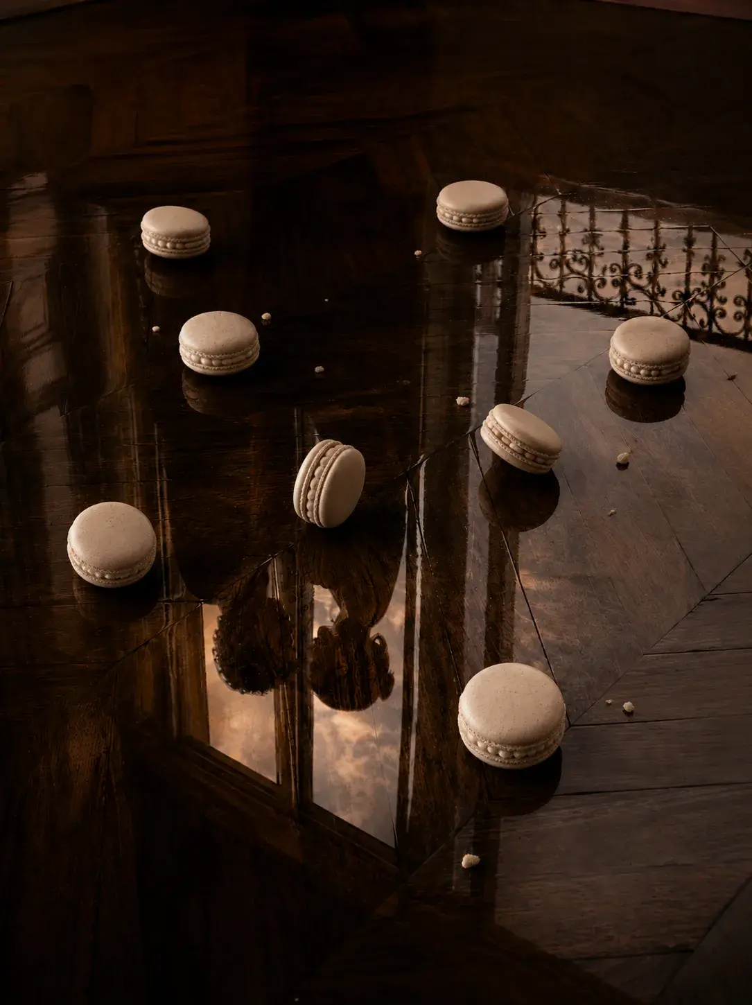 Vue plongeante sur parquet parisien lustré avec macarons blancs éparpillés et reflets, balustrade en fer forgé visible