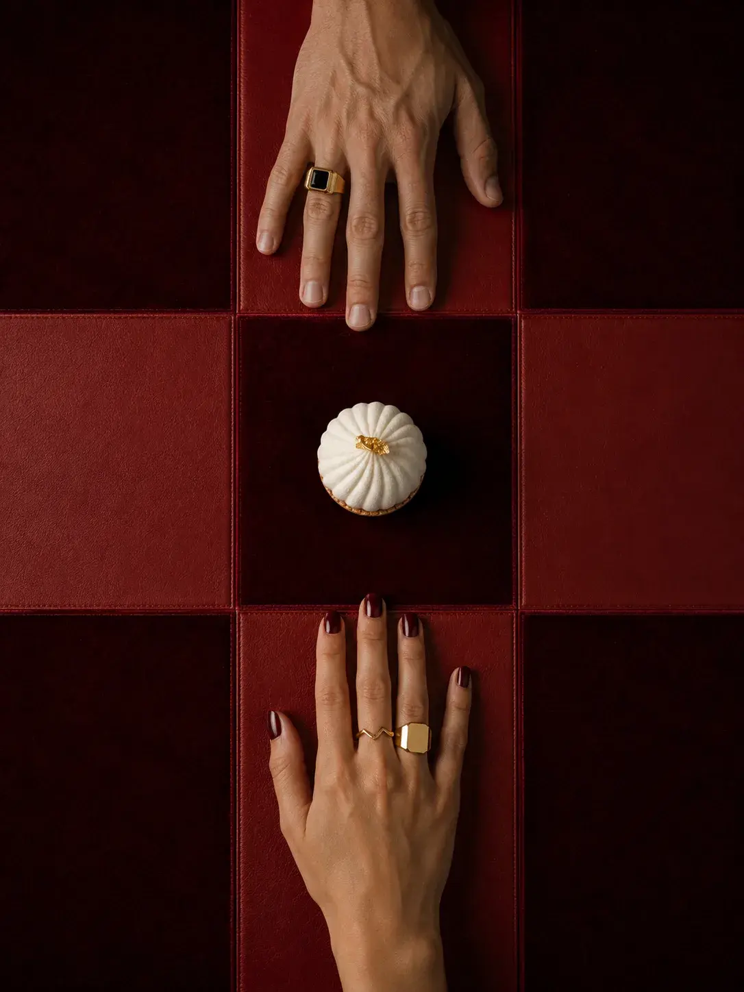 Vue plongeante symétrique sur deux paires de mains féminines aux bagues sur fond rouge à damier avec pâtisserie blanche au centre