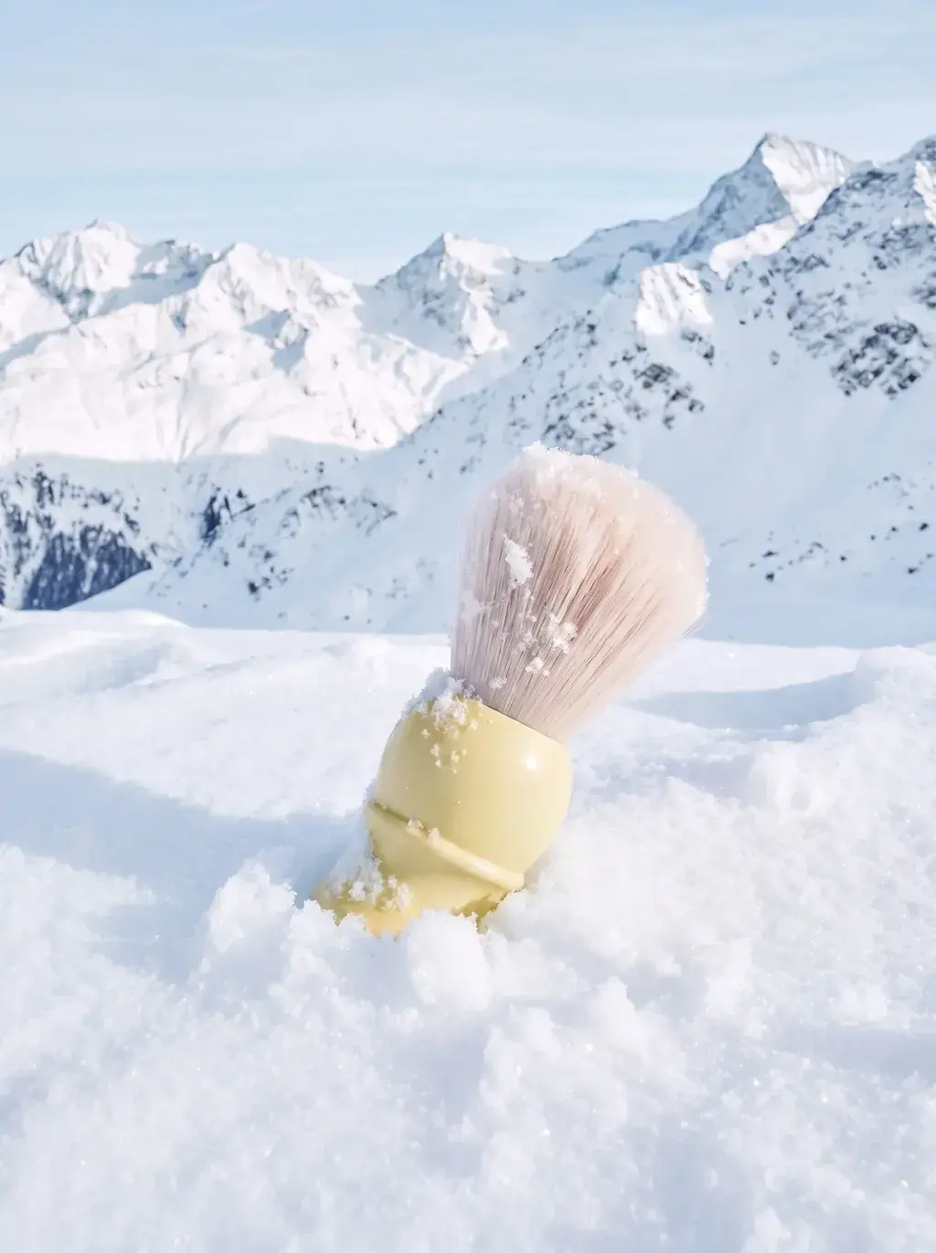 Gros plan d'un blaireau de rasage jaune enneigé planté dans la neige, montagnes en arrière-plan