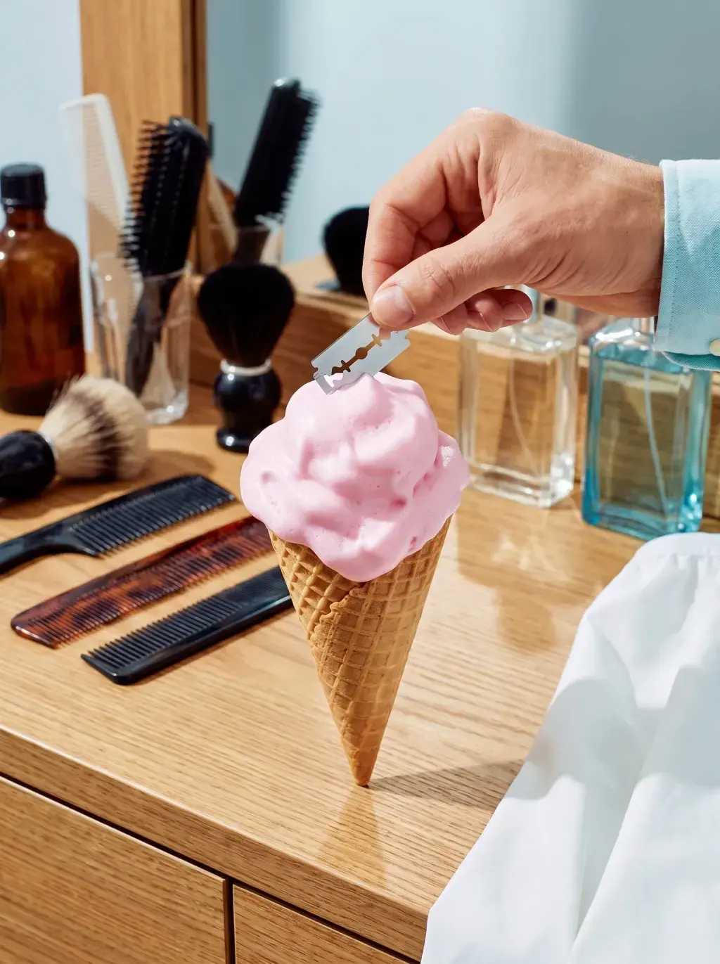 Main tenant une lame de rasoir posée sur un cornet façon glace à la mousse à raser, coiffeuse en bois