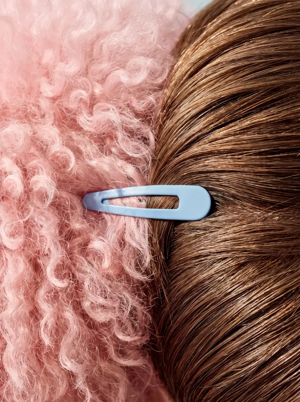 Gros plan d'une barrette bleu ciel dans une chevelure brune sur fond de fourrure bouclée rose