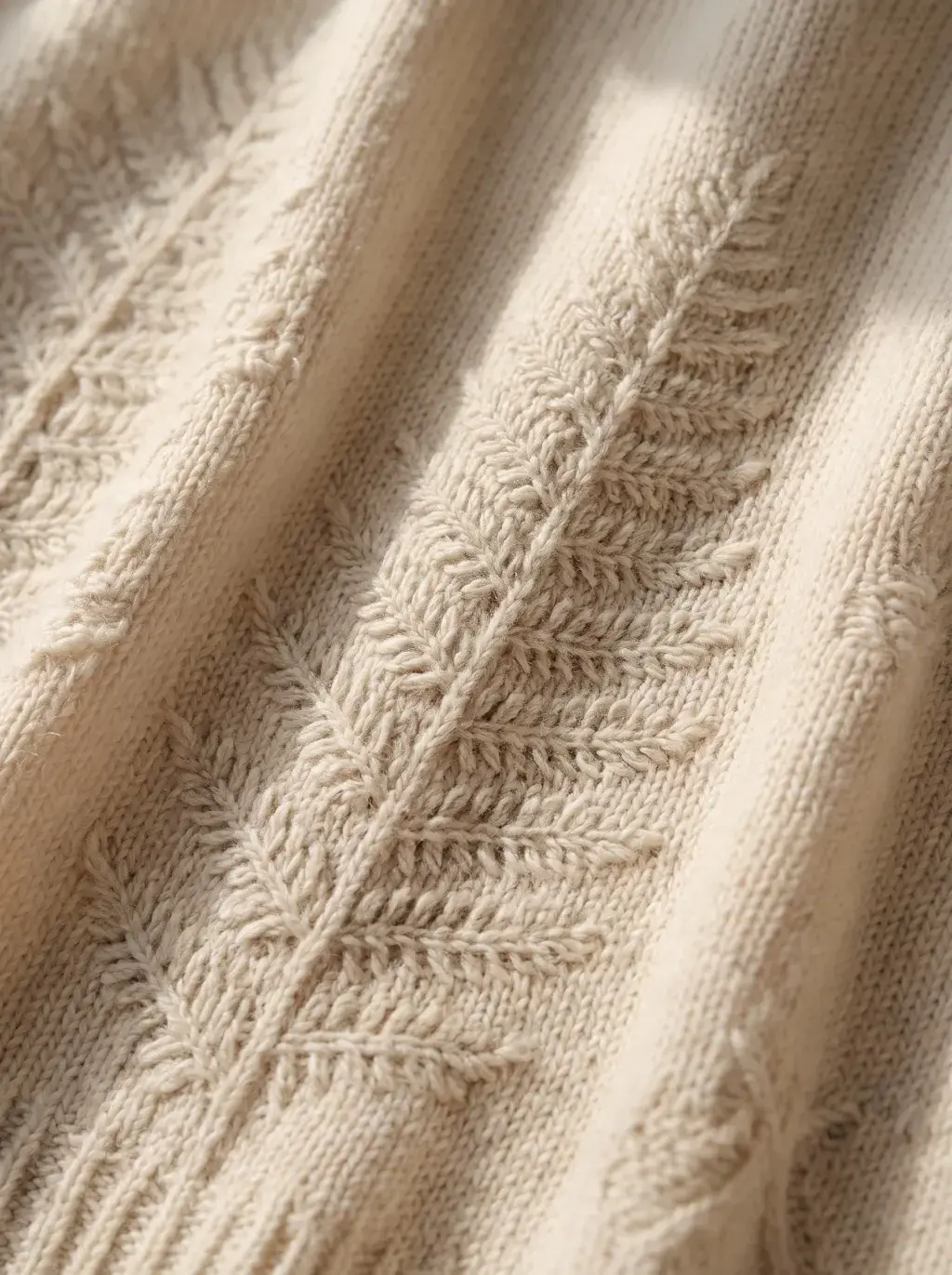 Gros plan sur un tricot côtelé crème orné d'un motif torsadé en feuille de fougère, éclairage latéral
